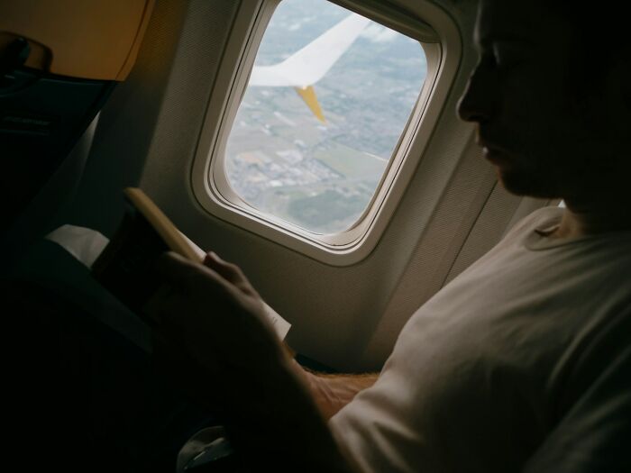 A passenger reading a book next to the window while on flights.