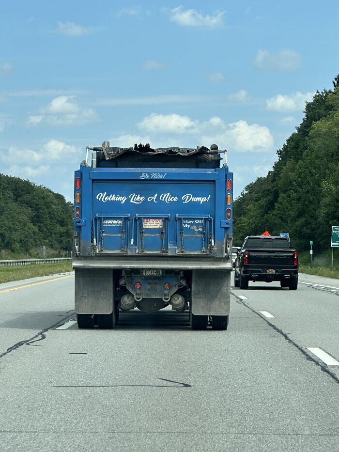 Blue dump truck on a highway with absurd signs painted on the back