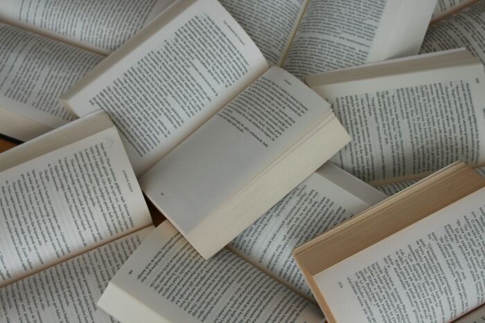 Pile of open books with visible printed text scattered on a surface