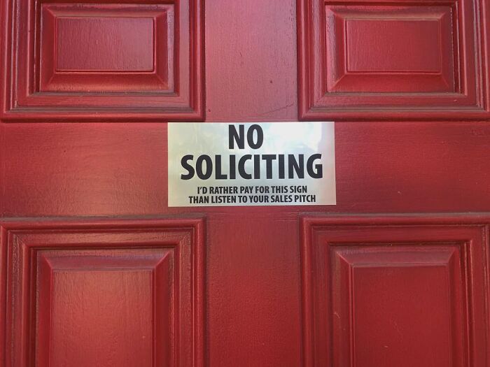Absurd signs mounted on a red front door reading No Soliciting with funny text