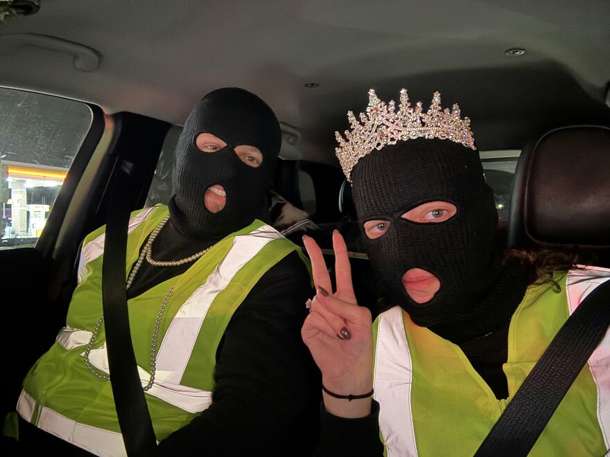 Couple in ski masks and safety vests sharing creative Halloween costume ideas in a car