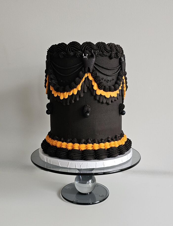 Tall black frosted Halloween cake decorated with intricate vintage-style piped black and orange buttercream swags.