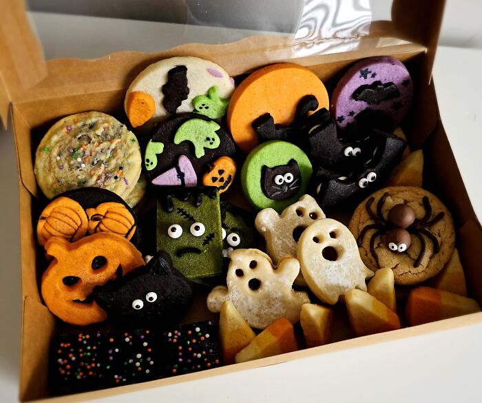 Assorted spooky Halloween foods arranged in a bakery box including ghost and pumpkin cookies