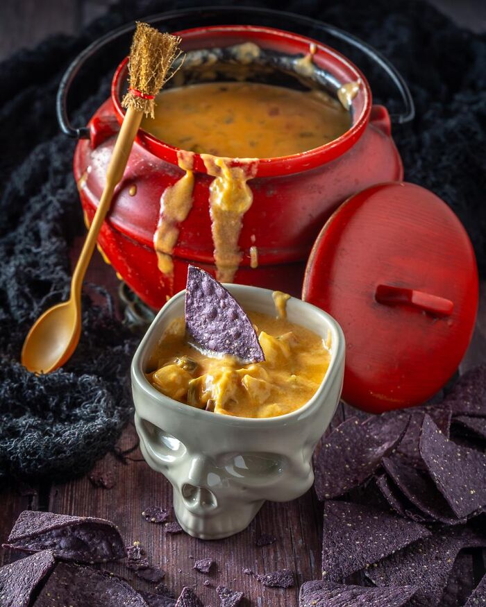 Spooky Halloween foods with cheese dip served in a red cauldron and skull cup.
