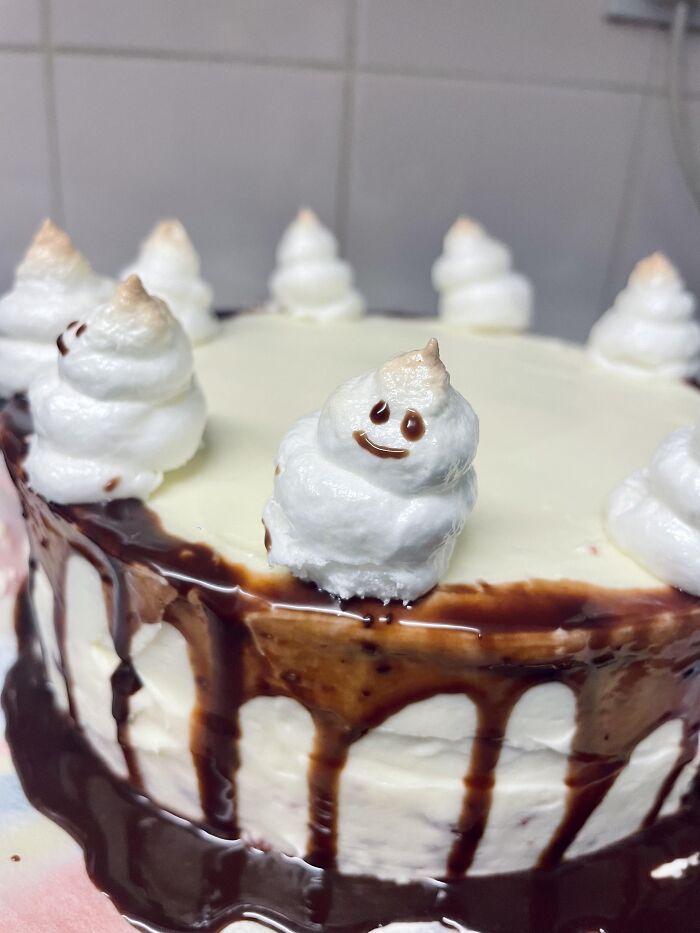 White frosted cake with chocolate drip and cute meringue ghosts as Halloween foods treats.