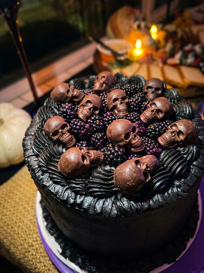 Dark chocolate Halloween foods cake topped with blackberries and detailed chocolate skull candies.