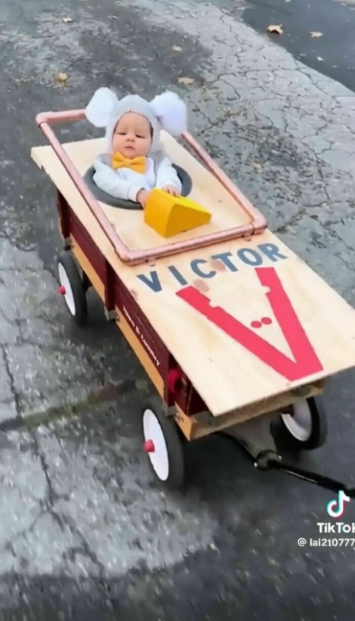 An adorable baby Halloween costume featuring a mouse sitting inside a custom wooden mousetrap wagon.