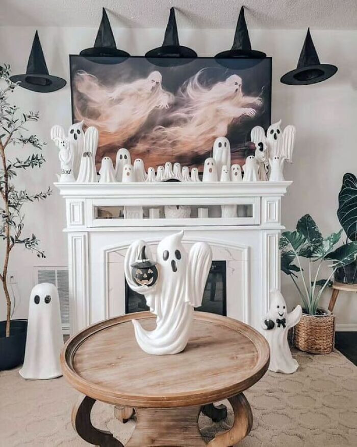 White fireplace mantle decorated with spooky ghost figurines and floating witch hats for Halloween.