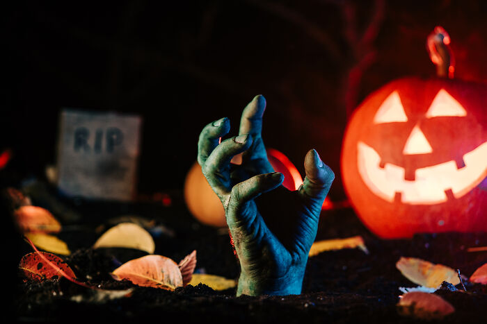 Zombie hand rising from the ground near a glowing Halloween pumpkin and tombstone