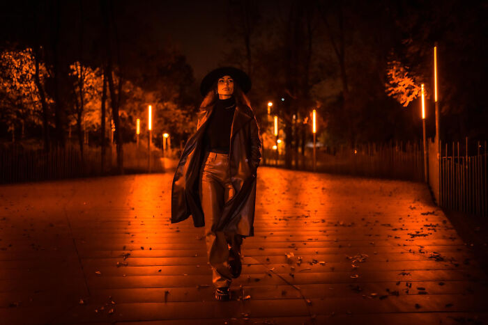 Woman in dark clothing walking through an eerie orange-lit haunted street