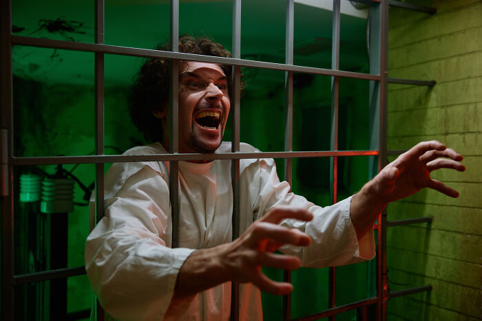 Man in straightjacket acting crazed behind jail bars in haunted house
