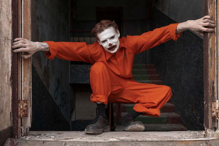 Creepy person in orange jumpsuit and clown makeup in a haunted house setting