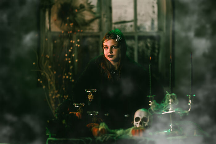 Girl dressed as witch in haunted house surrounded by candles and smoke