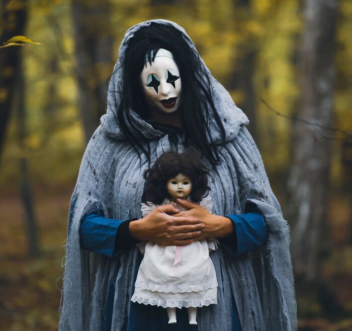 Figure in creepy clown mask holding doll in eerie forest haunt