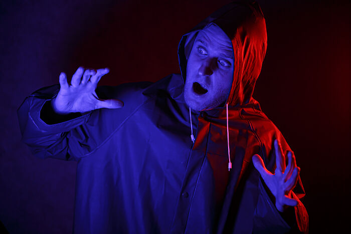 Scared man in red raincoat reacting to haunted house with blue lighting