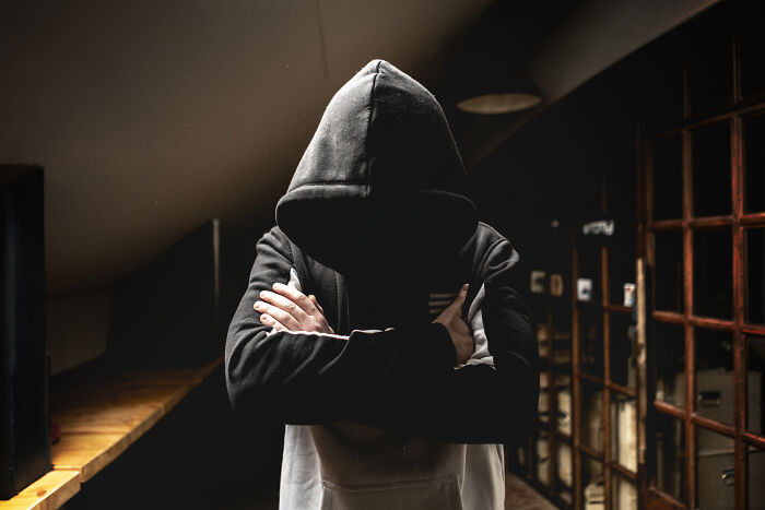 Mysterious hooded figure in dark room with arms crossed