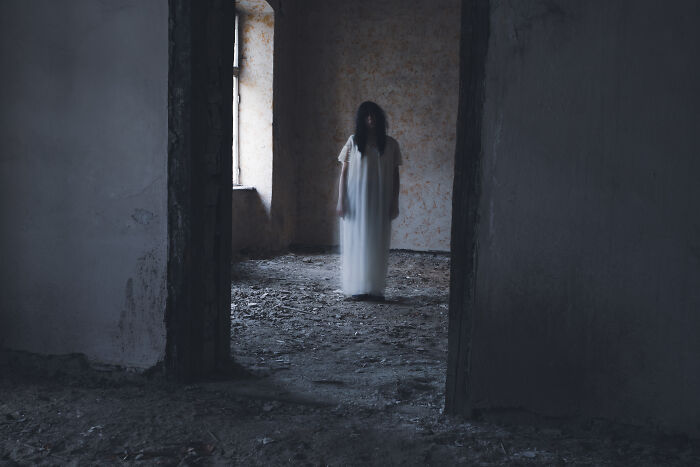 Ghostly figure in white dress standing in dark haunted house room