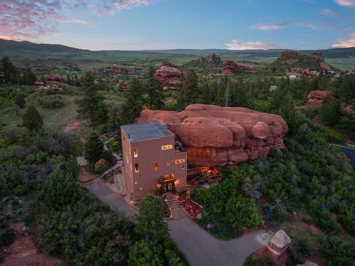 Unique cube-shaped building next to large red rocks in natural landscape