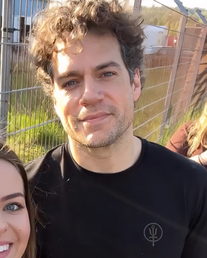 A recent photo of Henry Cavill with curly hair and a casual shirt, showing his five-year transformation.