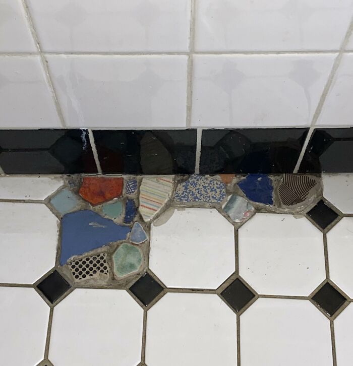 A tiled bathroom floor repaired with a mosaic of colorful broken ceramic pieces using creativity.