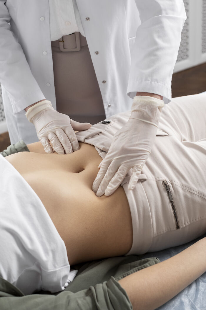 A doctor wearing gloves performing an abdominal exam on a patient to address health problems in Gen Z.