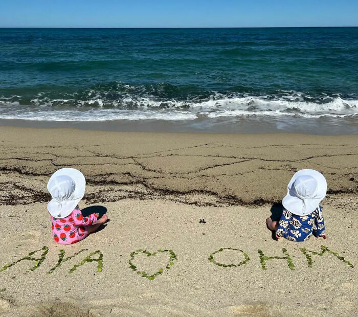 Two babies sitting on beach by ocean with names in sand Two babies sitting on beach by ocean with names in sand