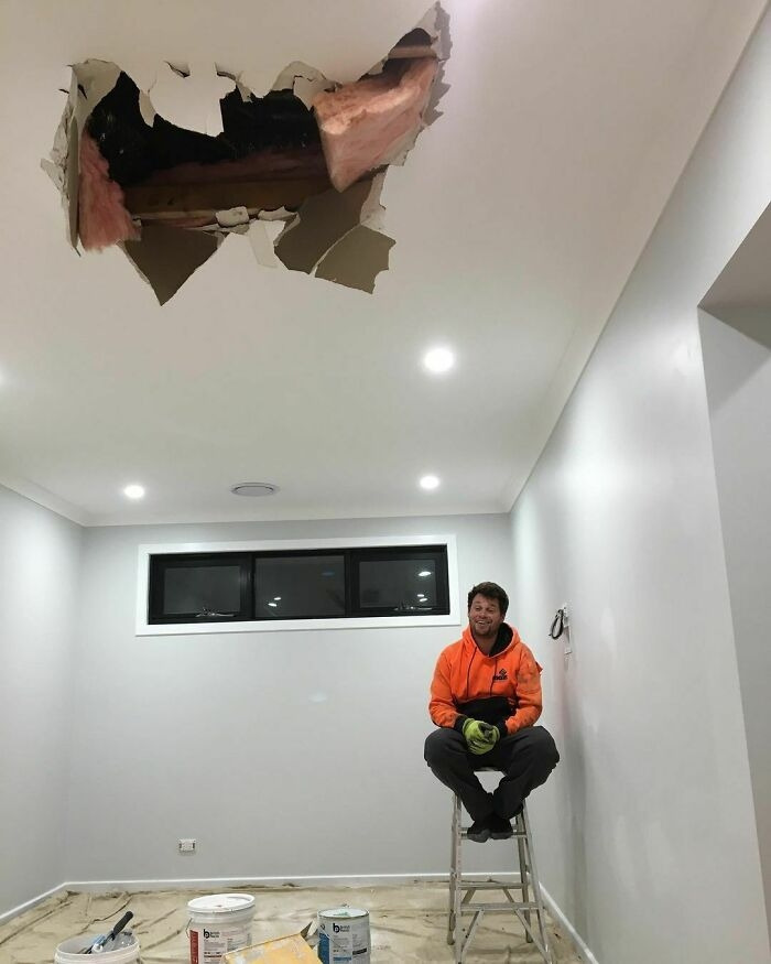 A worker sitting on a ladder beneath a giant hole in the ceiling during a home renovation