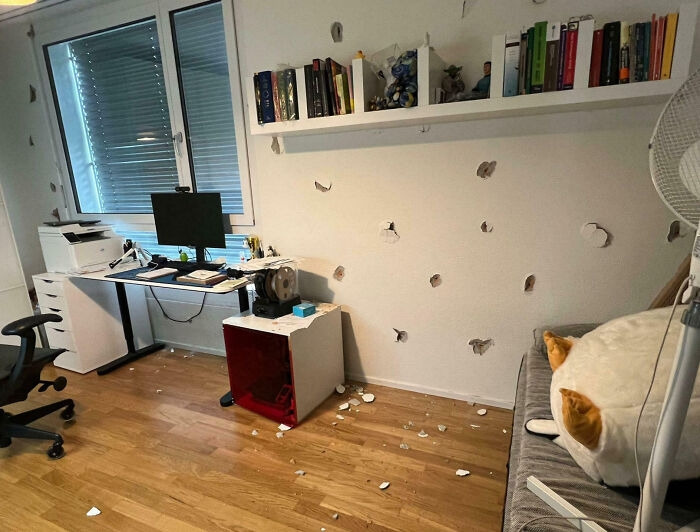 An office space with numerous holes in the wall, showing a DIY renovation fiasco with debris on the floor.