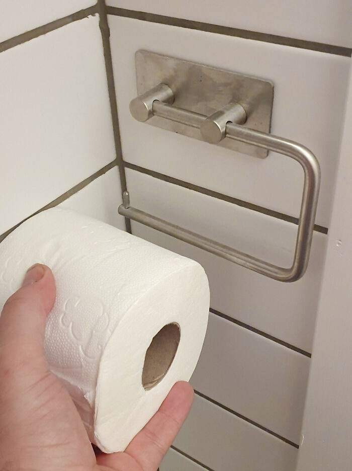 A poorly planned bathroom renovation fiasco with a toilet paper holder installed too close to a tiled wall.