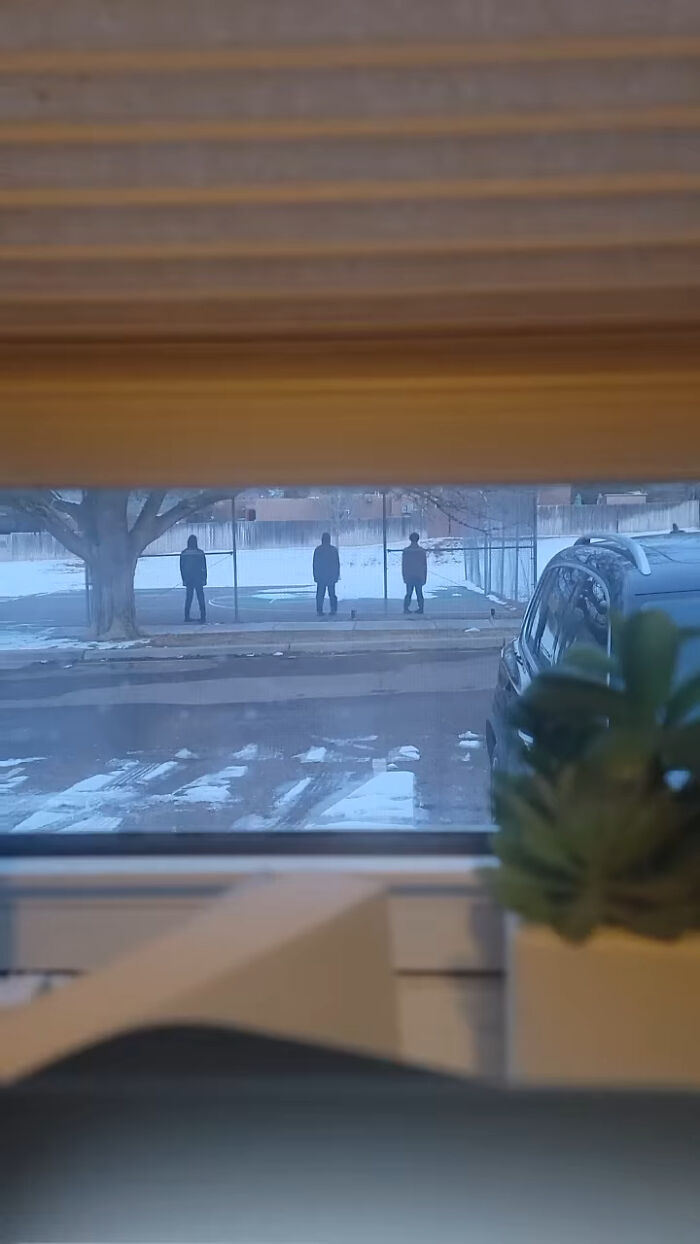 Creepy photos from a window showing three mysterious hooded figures standing in a snowy field at dusk.