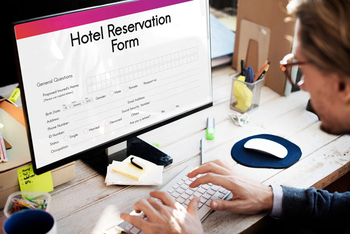 Man filling out hotel reservation form on computer at desk Man filling out hotel reservation form on computer at desk
