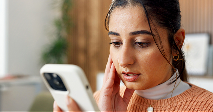 Worried woman looks at phone upset by husband's dating app profile discovery