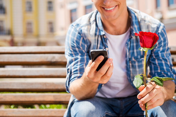 Man with rose smiling while using dating app on phone