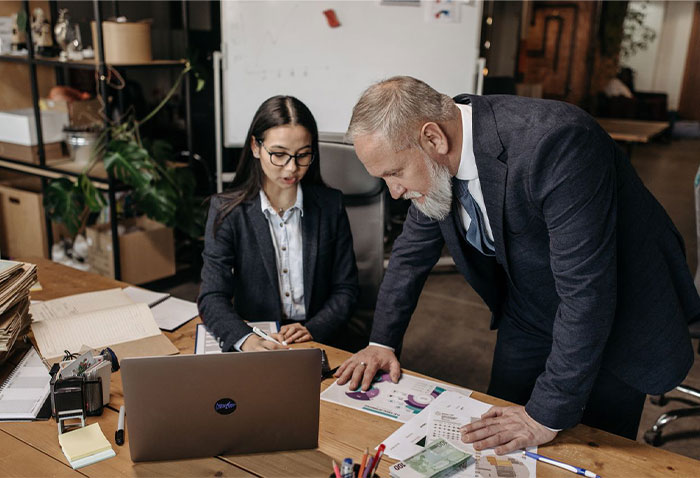 A senior male professional working alongside a young female 22YO assistant at a desk A senior male professional working alongside a young female 22YO assistant at a desk