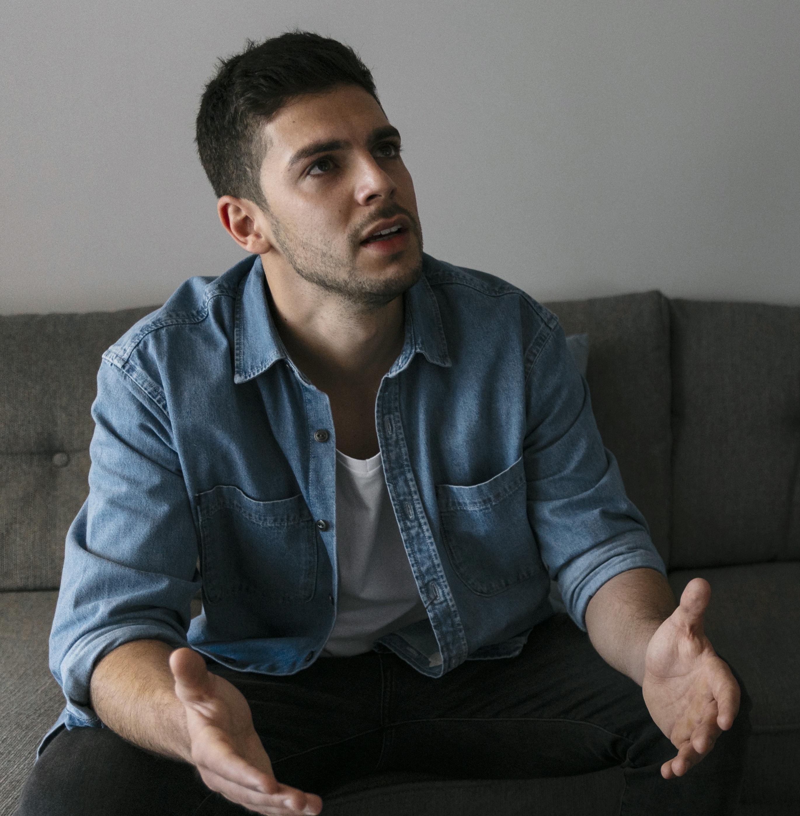 A panicking BF sitting on a couch with open arms explaining himself. A panicking BF sitting on a couch with open arms explaining himself.