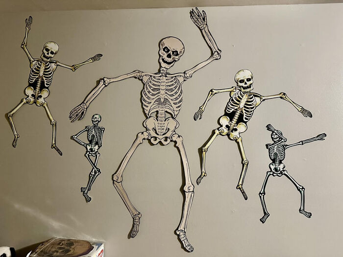 Paper skeletons in funny poses on a wall for Halloween decor.