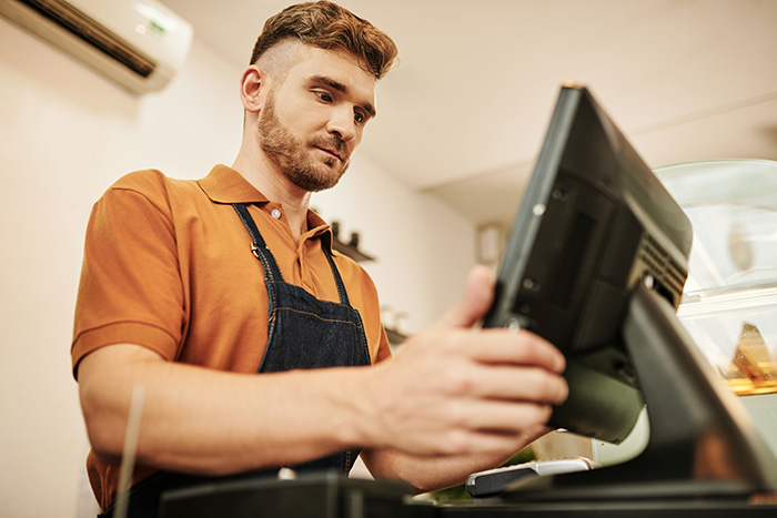 Young male store clerk operating a cash register in retail Young male store clerk operating a cash register in retail