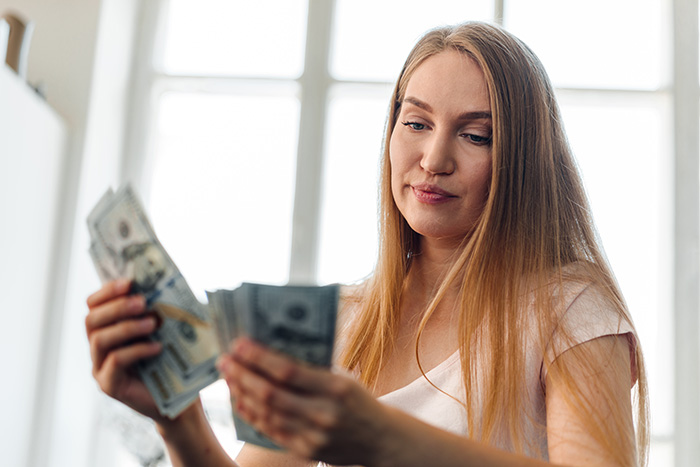 A woman holding and counting US dollar bills after an aunt sends a payment request for past favors. A woman holding and counting US dollar bills after an aunt sends a payment request for past favors.
