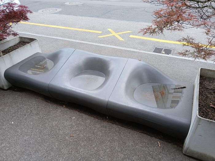 A grey outdoor bench with sunken seats filled with rainwater, showing one of many absurd products and moments.