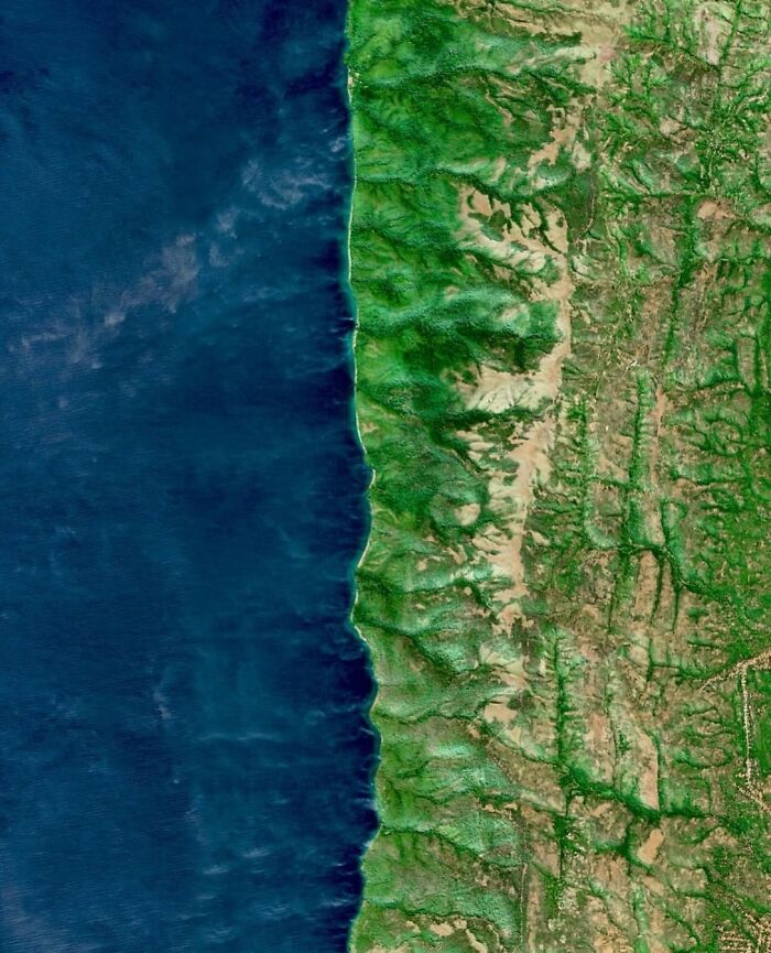 A high-angle satellite photo displaying a vibrant green coastline bordered by deep blue ocean waters.