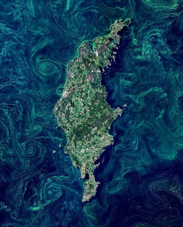 Satellite photo showing an island surrounded by swirling green ocean currents.