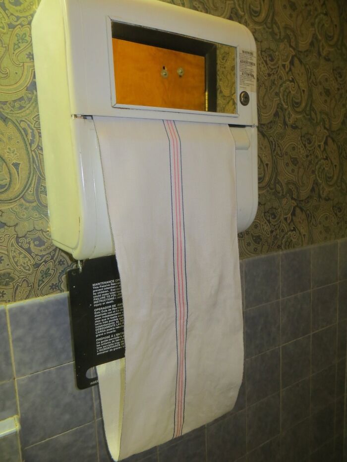 Antique fabric towel dispenser mounted on wall with paisley wallpaper