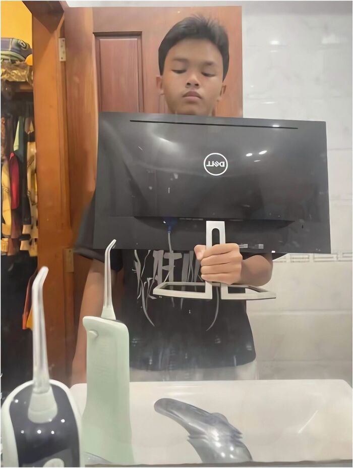 A boy taking a mirror selfie using a computer monitor in a bathroom, featured in amusing posts.