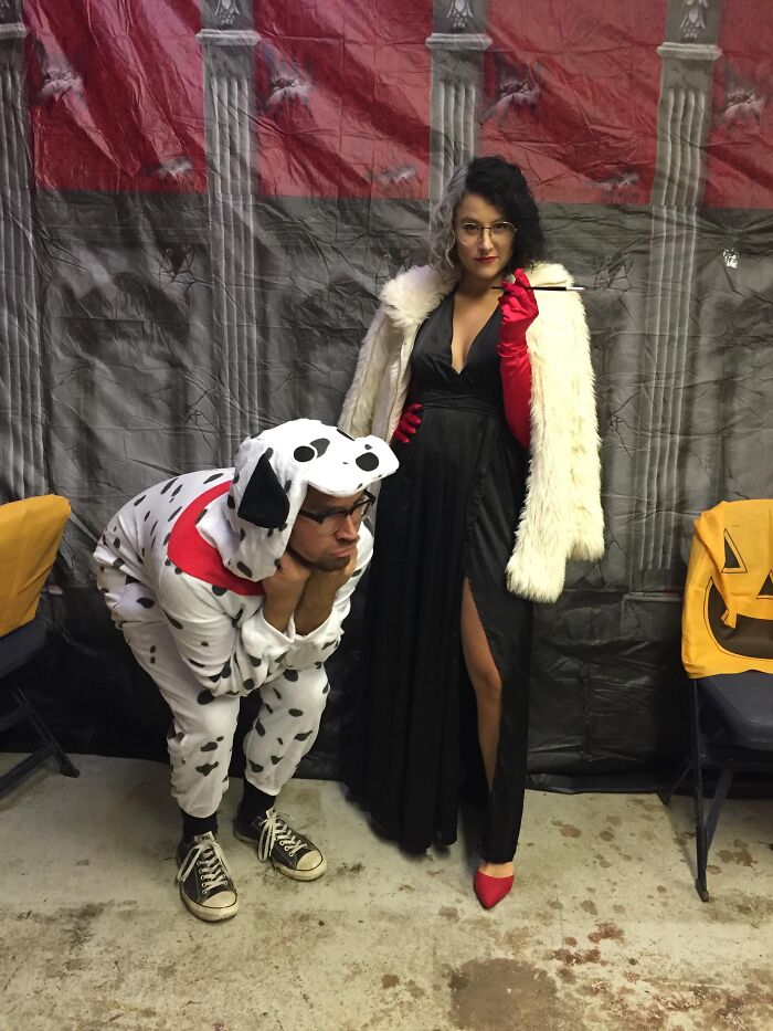 Funny Halloween couples costume with Cruella de Vil posing next to a person dressed in a Dalmatian dog suit