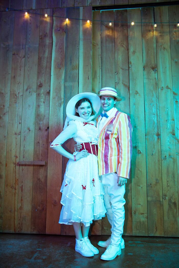 A couple posing in vintage Mary Poppins themed Halloween couples costumes in front of a wooden wall