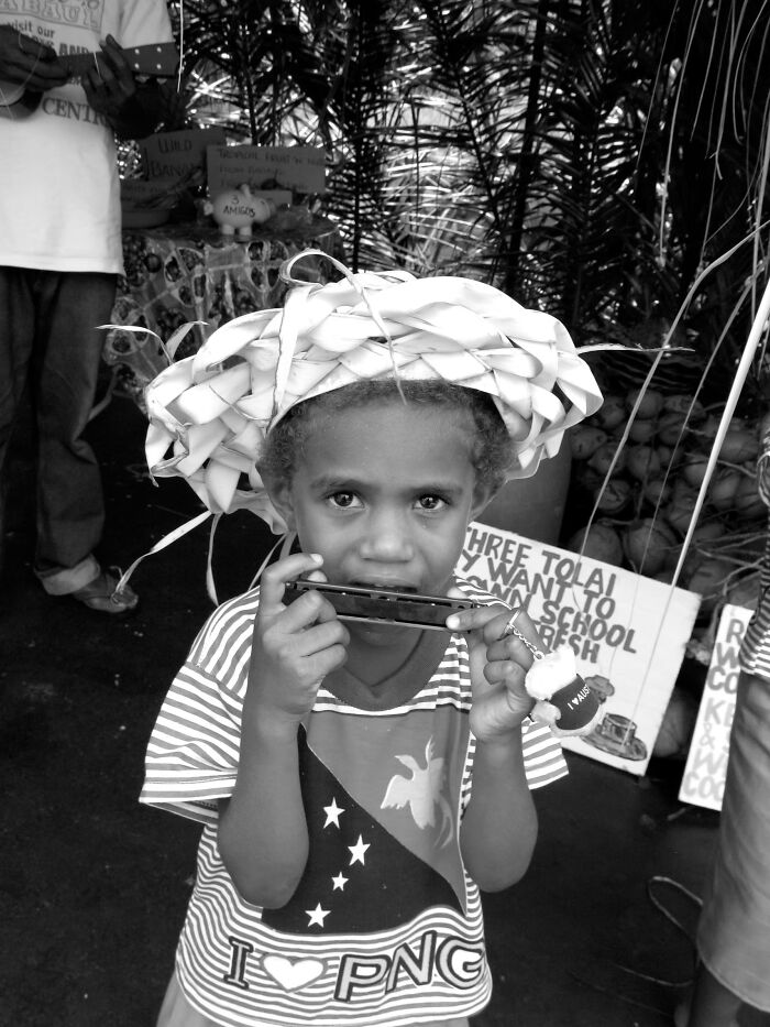 A black and white portrait photo of a young child wearing a woven hat playing a mouth harmonica