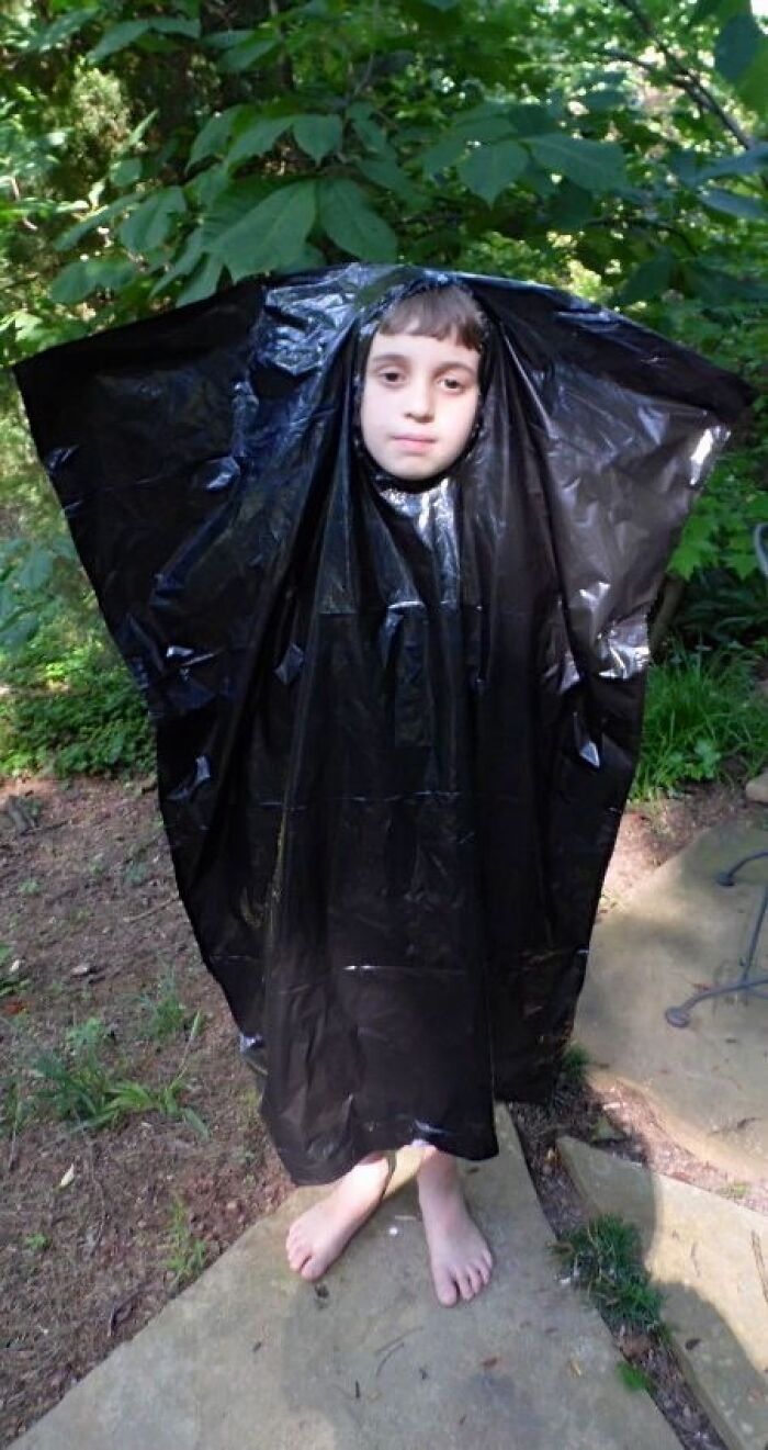 Funny Halloween photo of a kid wearing a black trash bag as a budget costume outdoors.