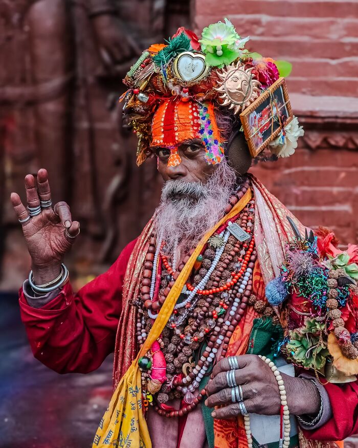 Vibrant portrait photos of a Sadhu in Nepal wearing a colorful headpiece and red robes making a hand gesture