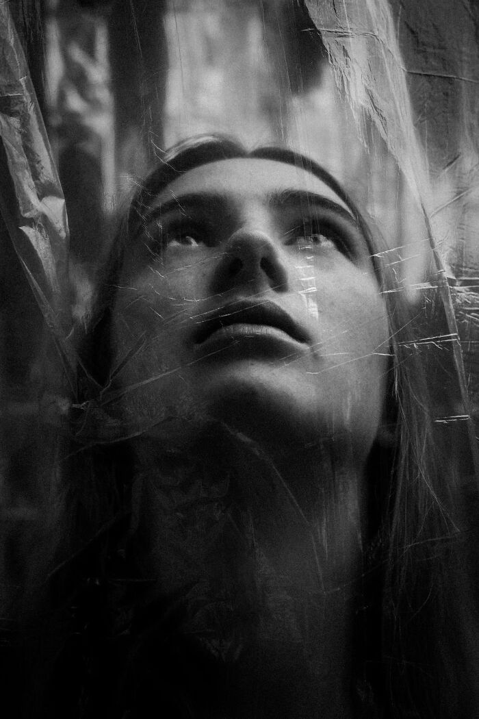 Dramatic black and white portrait photos showing a face looking upwards from behind a sheer plastic sheet