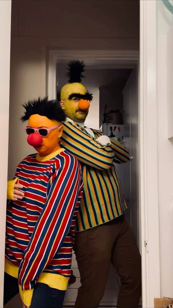 Bert and Ernie in striped sweaters as cool Halloween couples costumes posing together indoors.